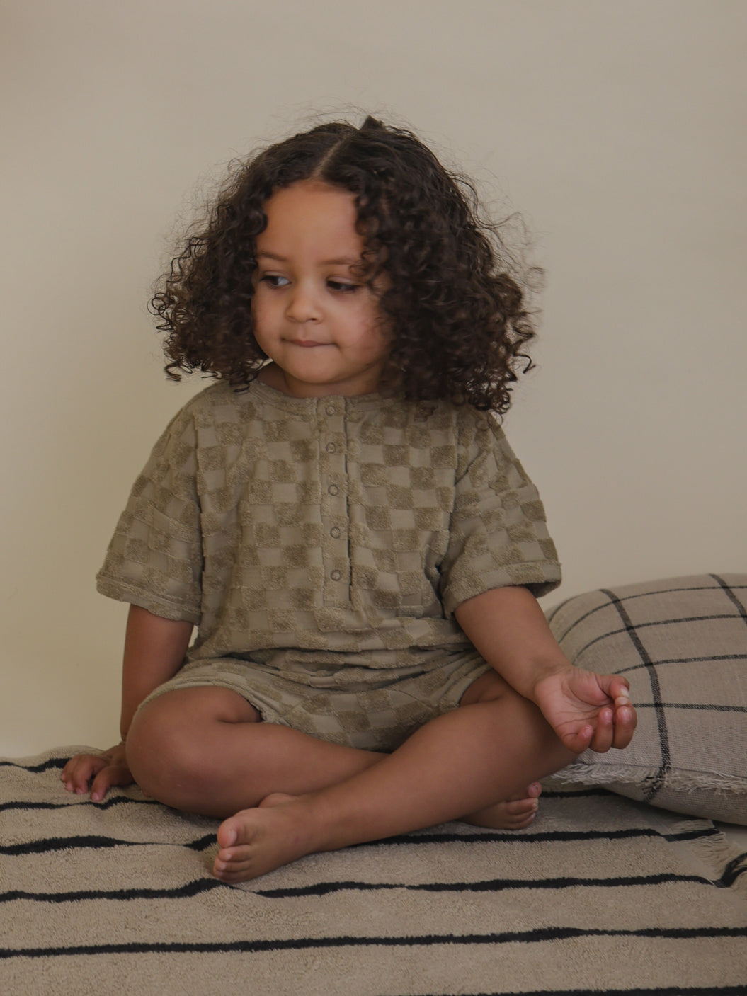 toddler wearing organic terry cotton romper with beige checkerboard pattern & front poppers sitting
