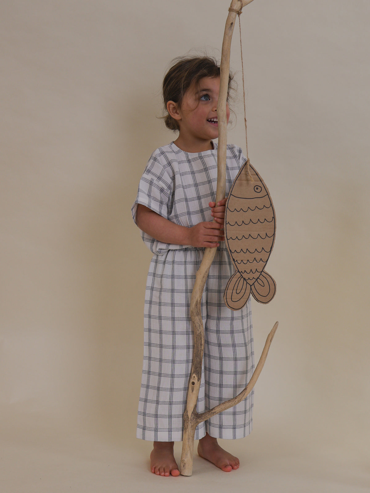 toddler in navy window check wide leg muslin pants & matching top holding branch with cardbox fish