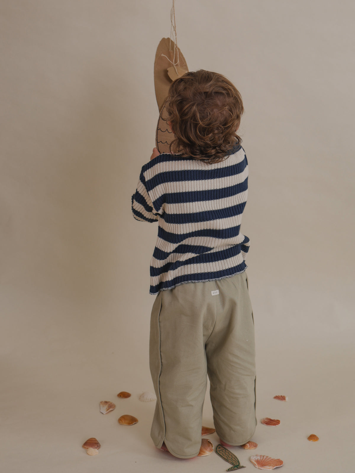 back view of toddler in seasalt grey balloon pants & stripes sweater, playing with cardboard fishes