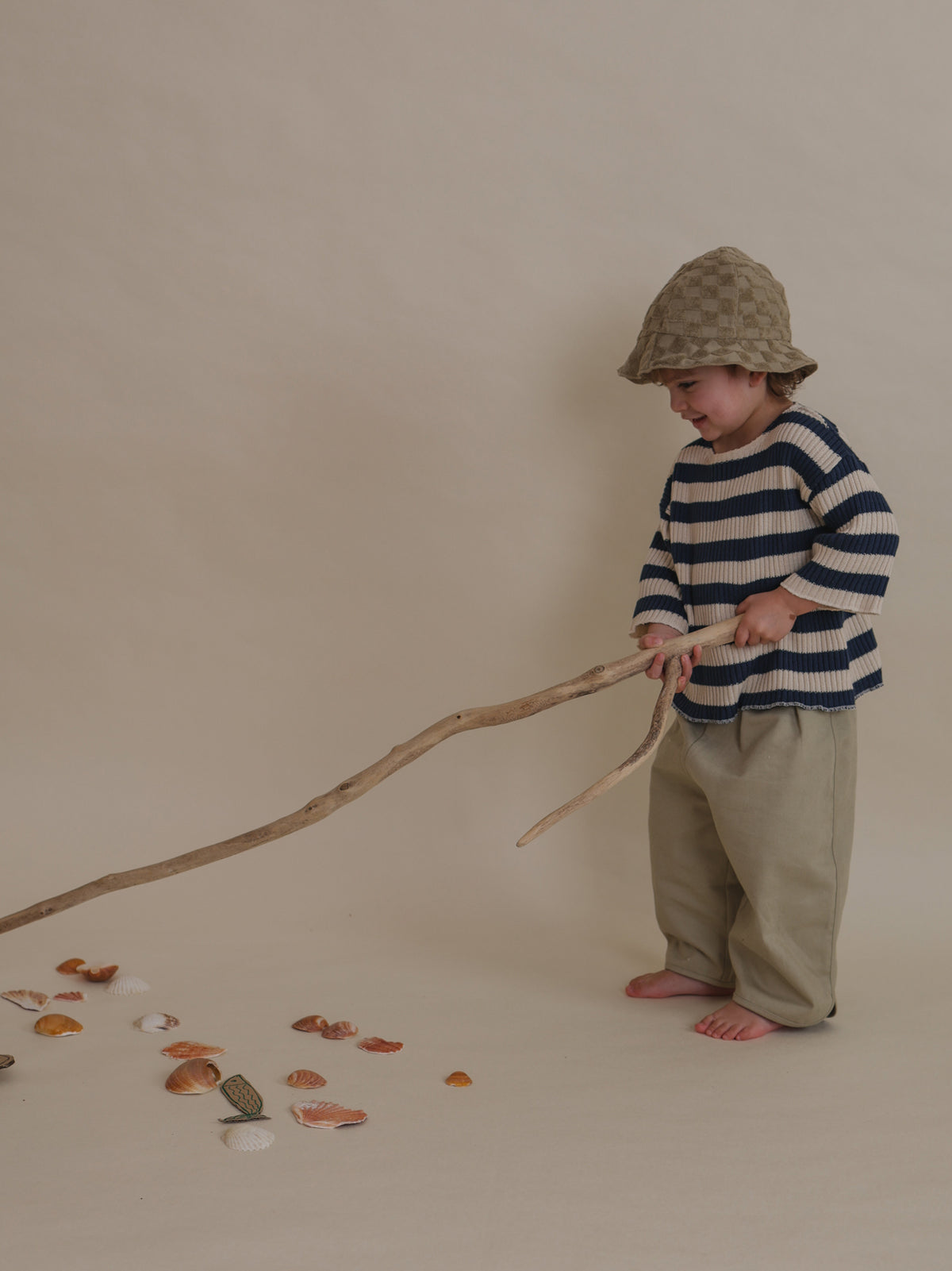 toddler dusky beige terry sun hat with checkerboard pattern playing with branch