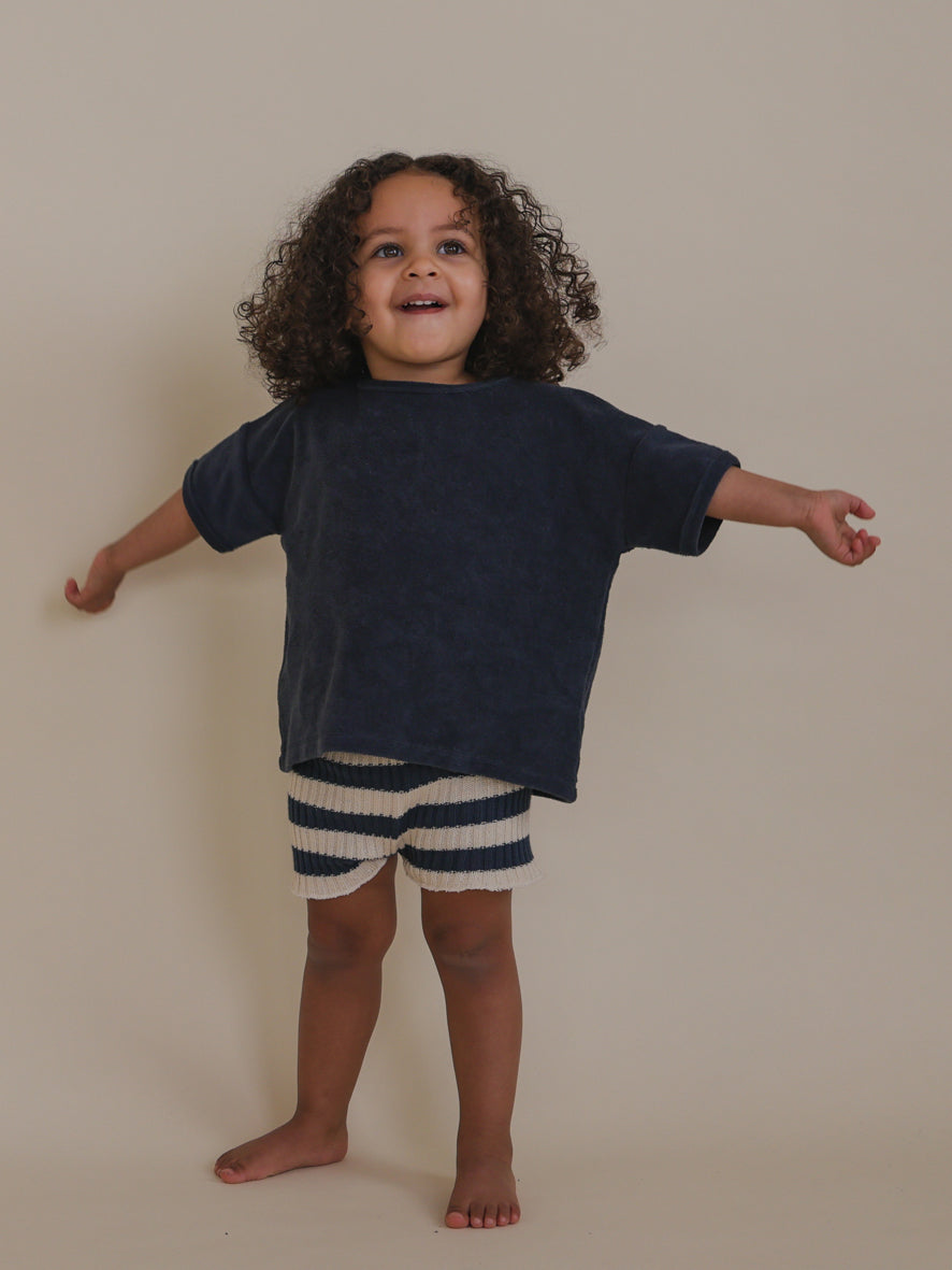 cheerful toddler wearing drop shoulder t-shirt in navy & stripes shorts standing with arms wide open