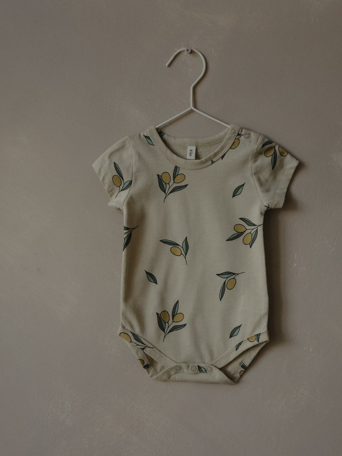 short sleeve baby bodysuit in cream with olives on hanger