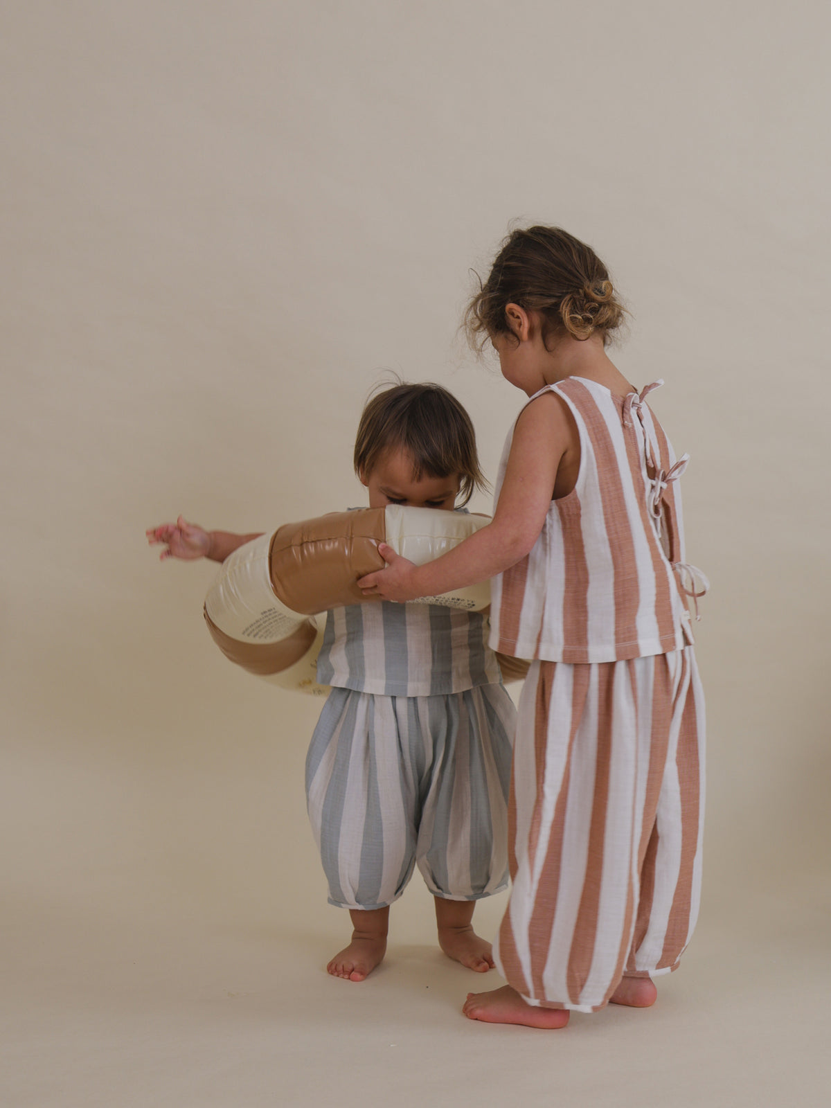 child in sienna red striped ribbon-tie back resort muslin top & pants putting pool ring on toddler