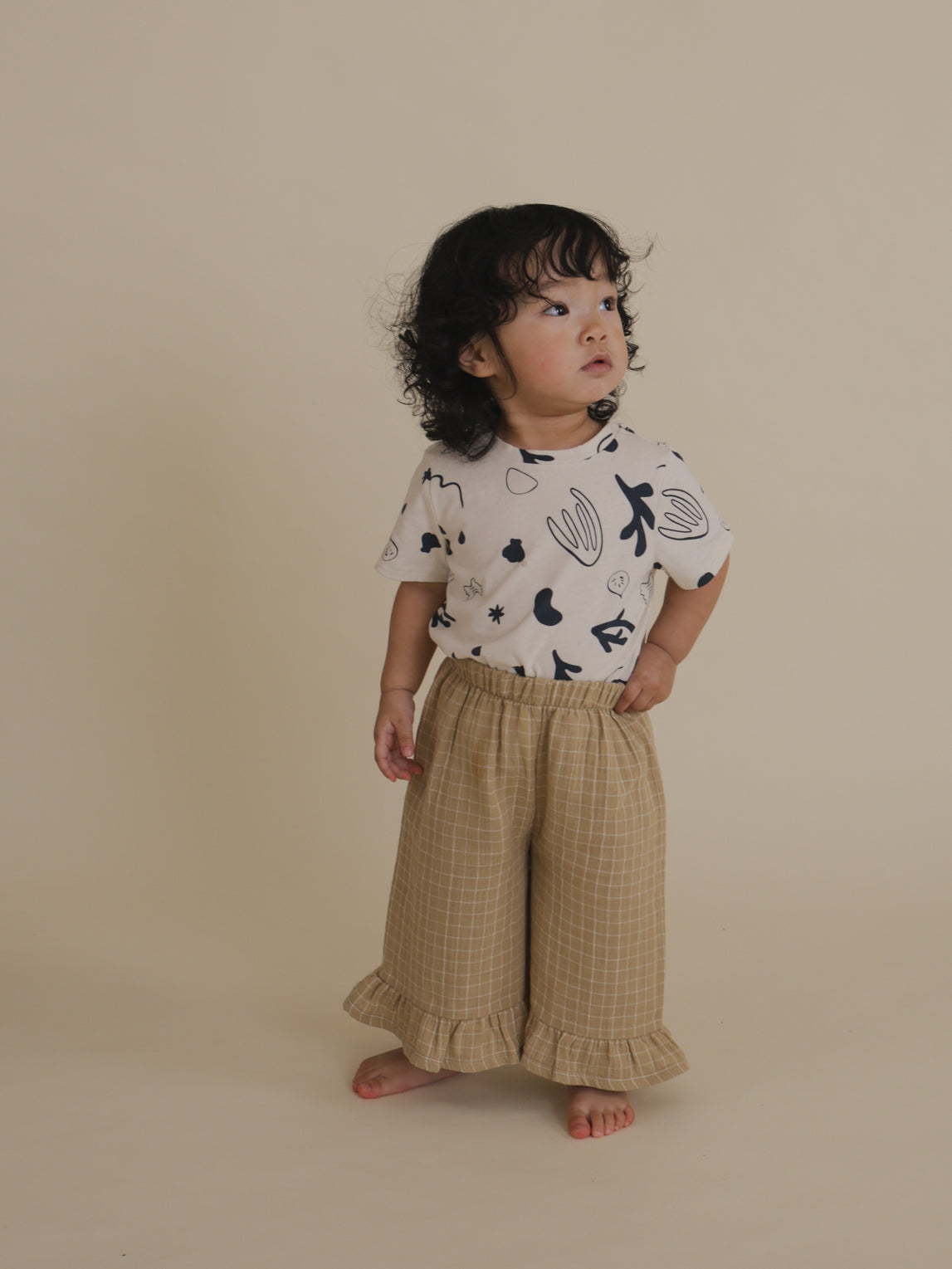 toddler wearing crew neck t-shirt with ocean print tucked into pants, with one hand on waist