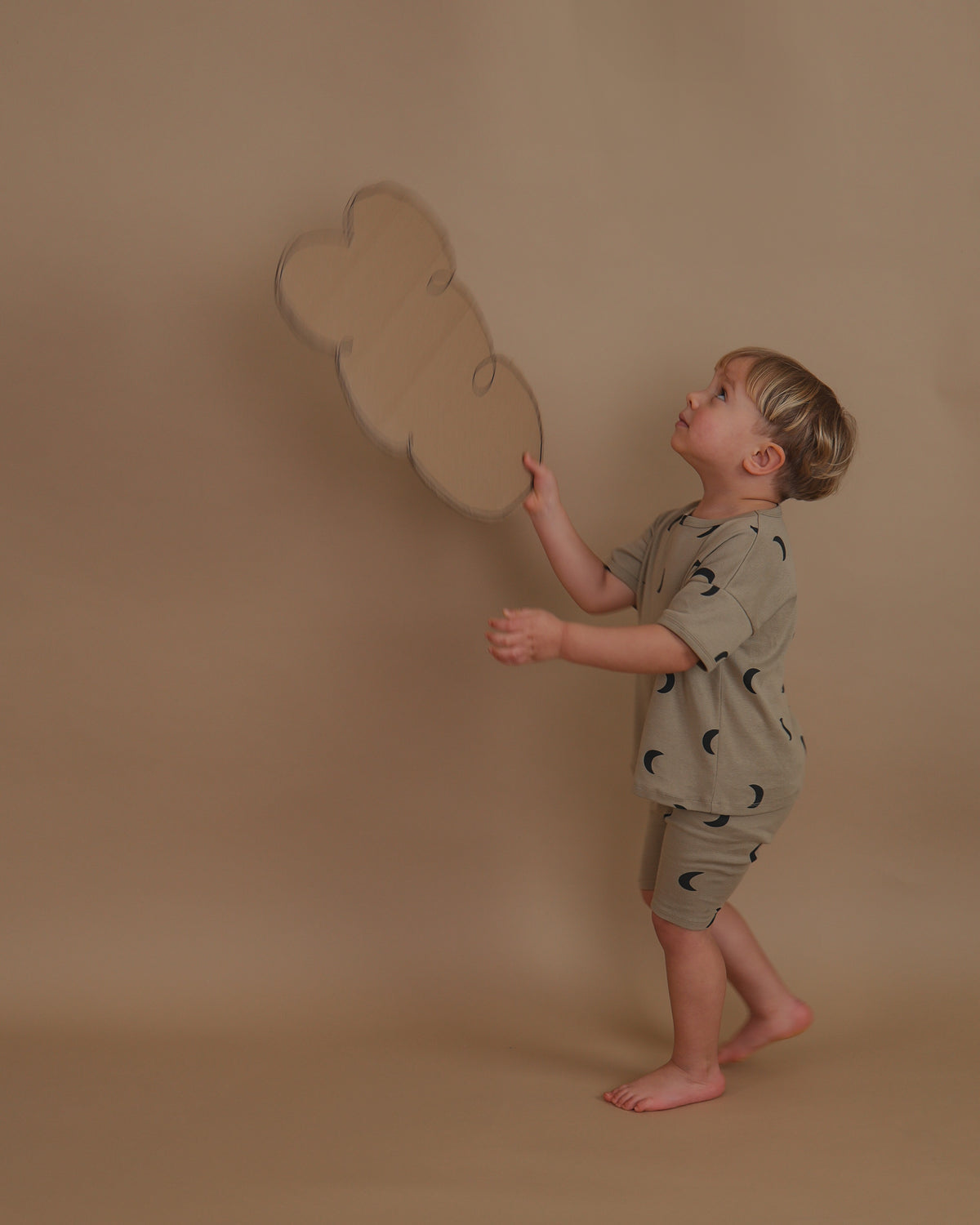toddler in ribbed cotton boxy t-shirt in beige with moon print playing with cardboard cloud