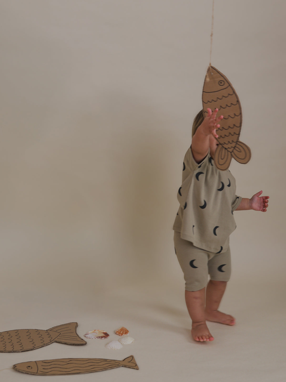 toddler in ribbed cotton dusky beige boxy t-shirt with moon print reaching for cardboard fish
