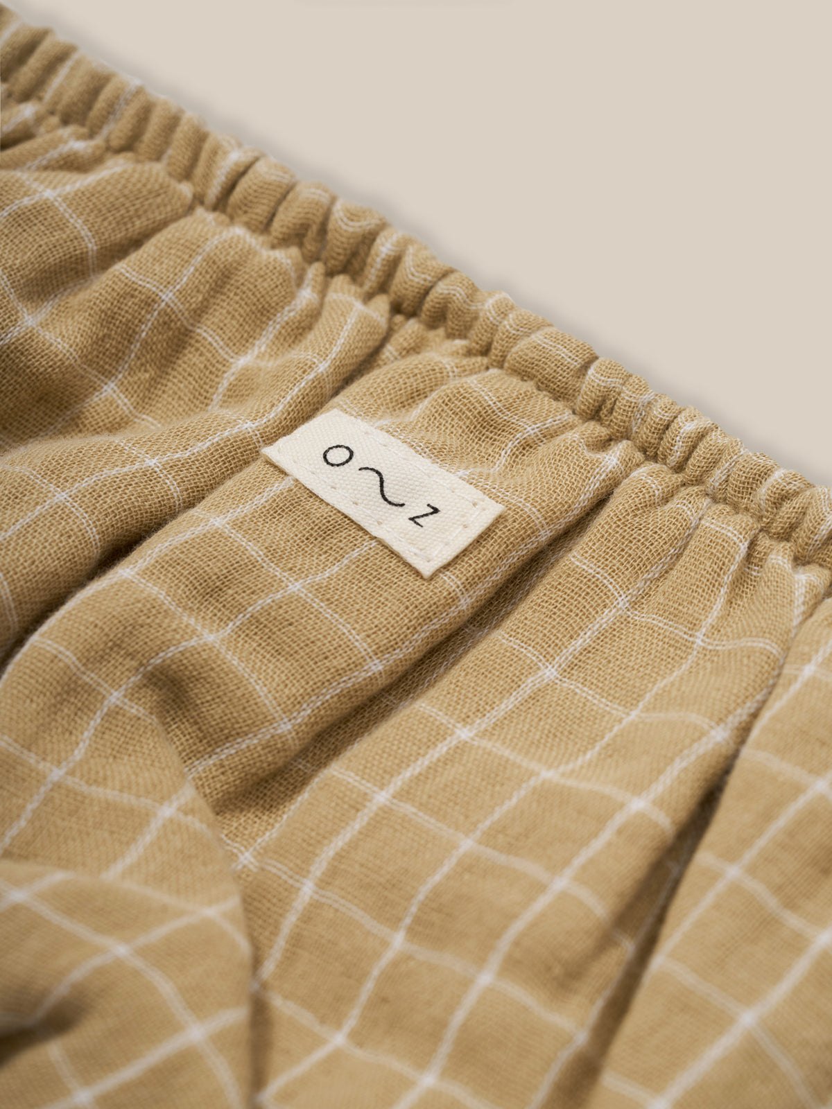 close up of baby & toddler organic muslin shortie in wheat gold grid check pattern