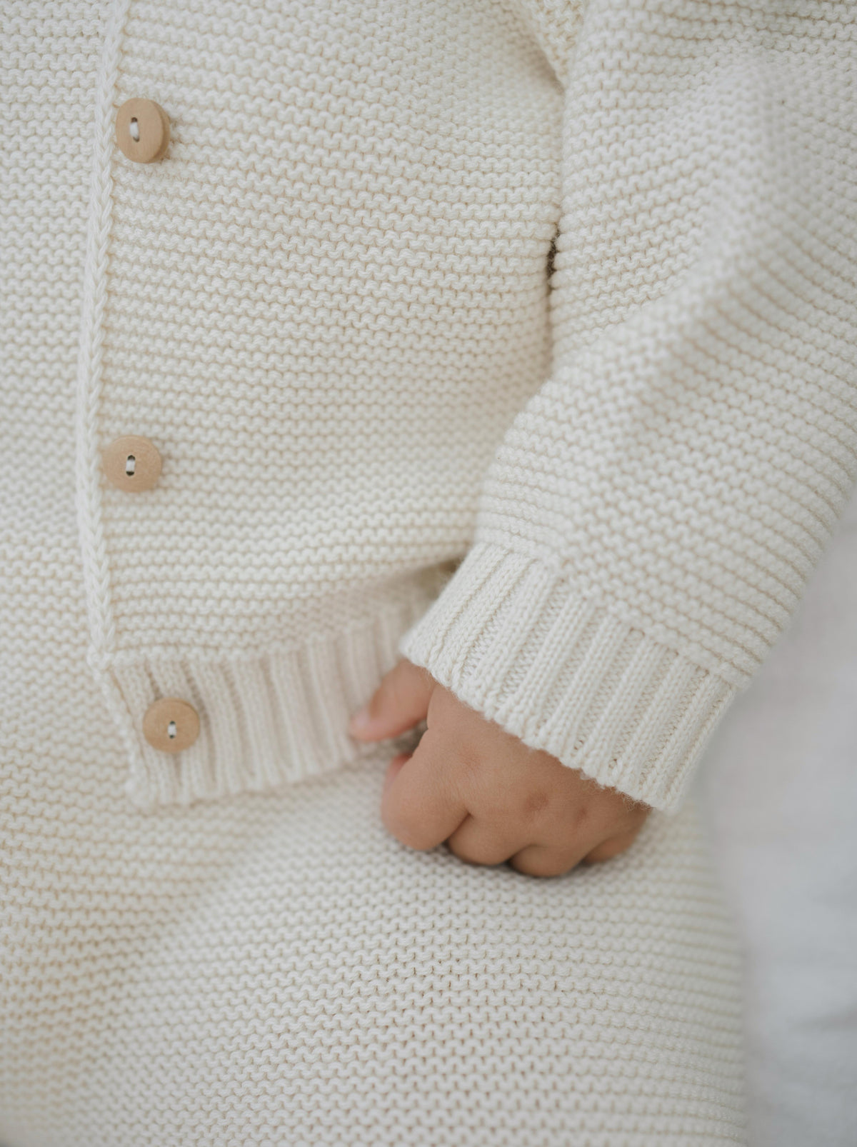 close up of baby wearing matching cream knitted button down cardigan and salopette