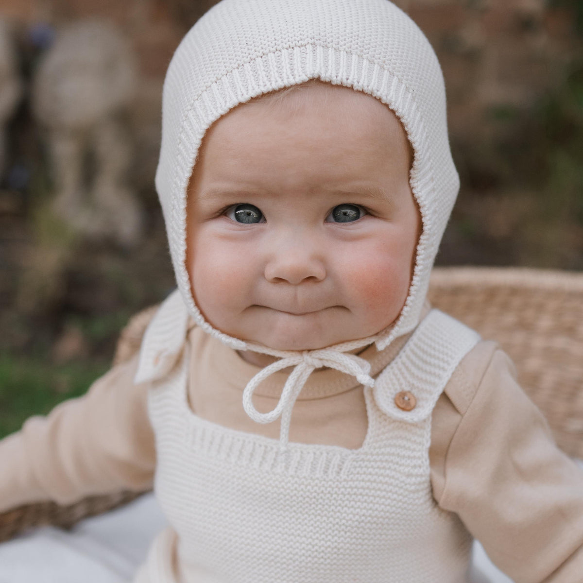 happy baby in knitted cotton pixie hat with chin tie, sitting in moses basket