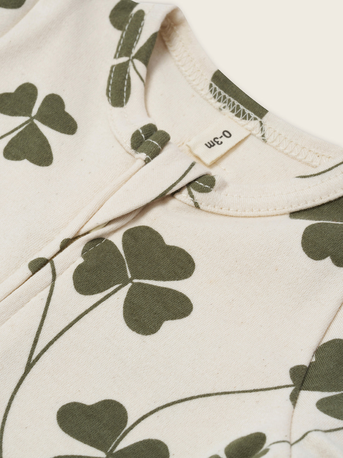 close up of baby cream undyed cotton zip sleepsuit with green clover print