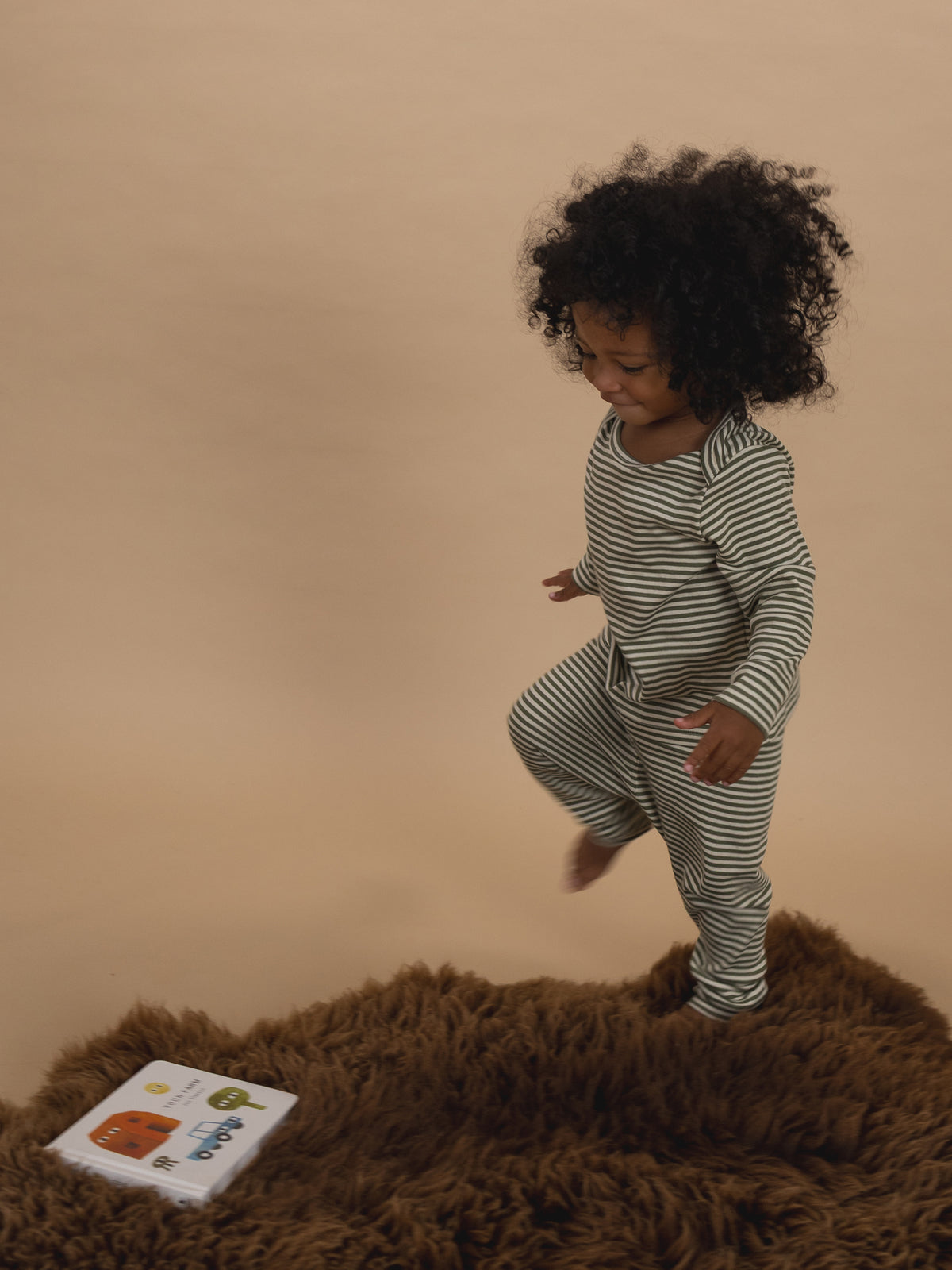 toddler in ribbed cotton long-sleeved top & leggings set in green & cream stripes, hopping on rug