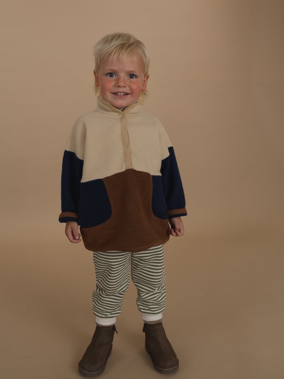 toddler in fern green and white striped sweatpants, colour block sweater, and boots