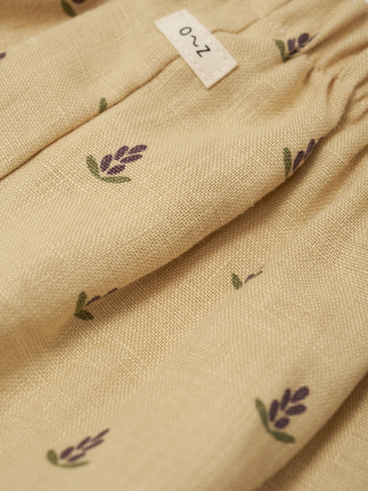 Beige fabric with lavender designs and a label on a beige background