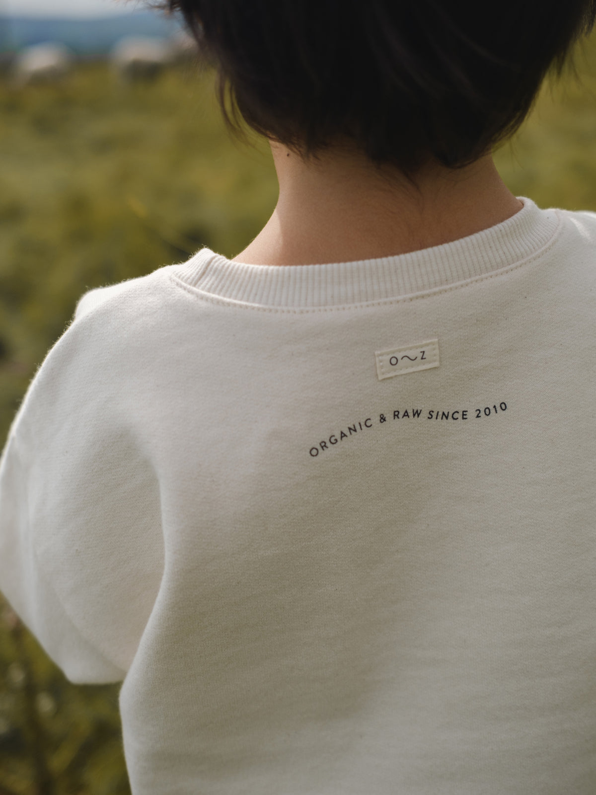back view of toddler in cream undyed cotton sweatshirt with O~Z label and ‘Organic & Raw Since 2010’ text