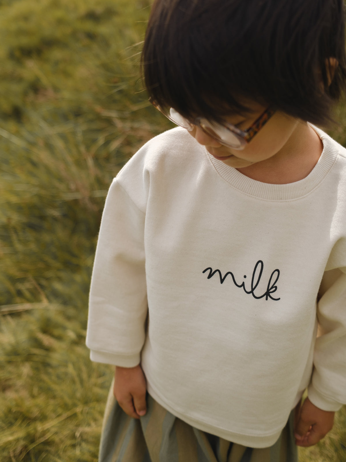 toddler in cream undyed cotton boxy drop shoulder sweatshirt with milk text standing in field