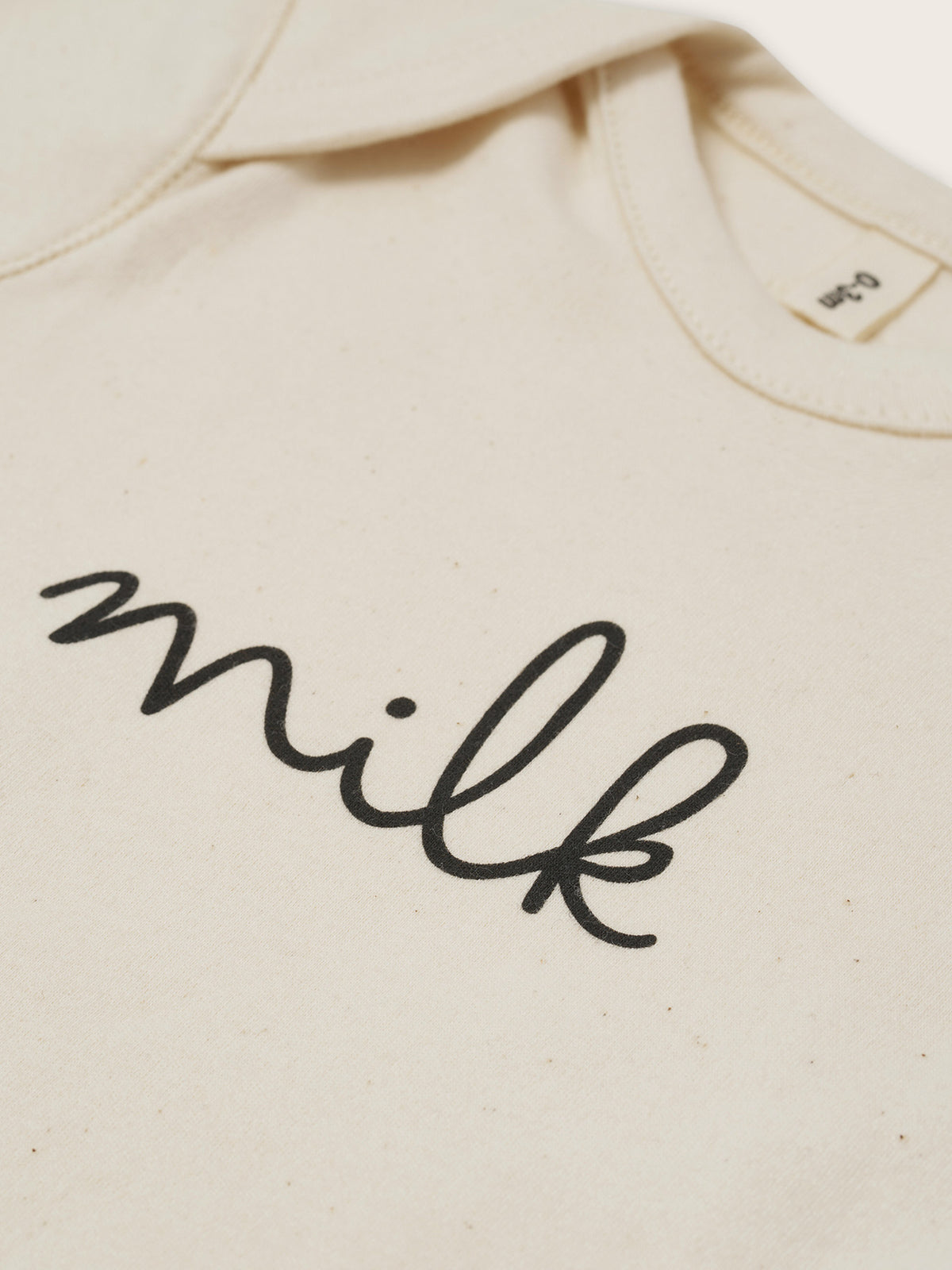 close up of baby cream undyed cotton playsuit with milk text, and envelope shoulders