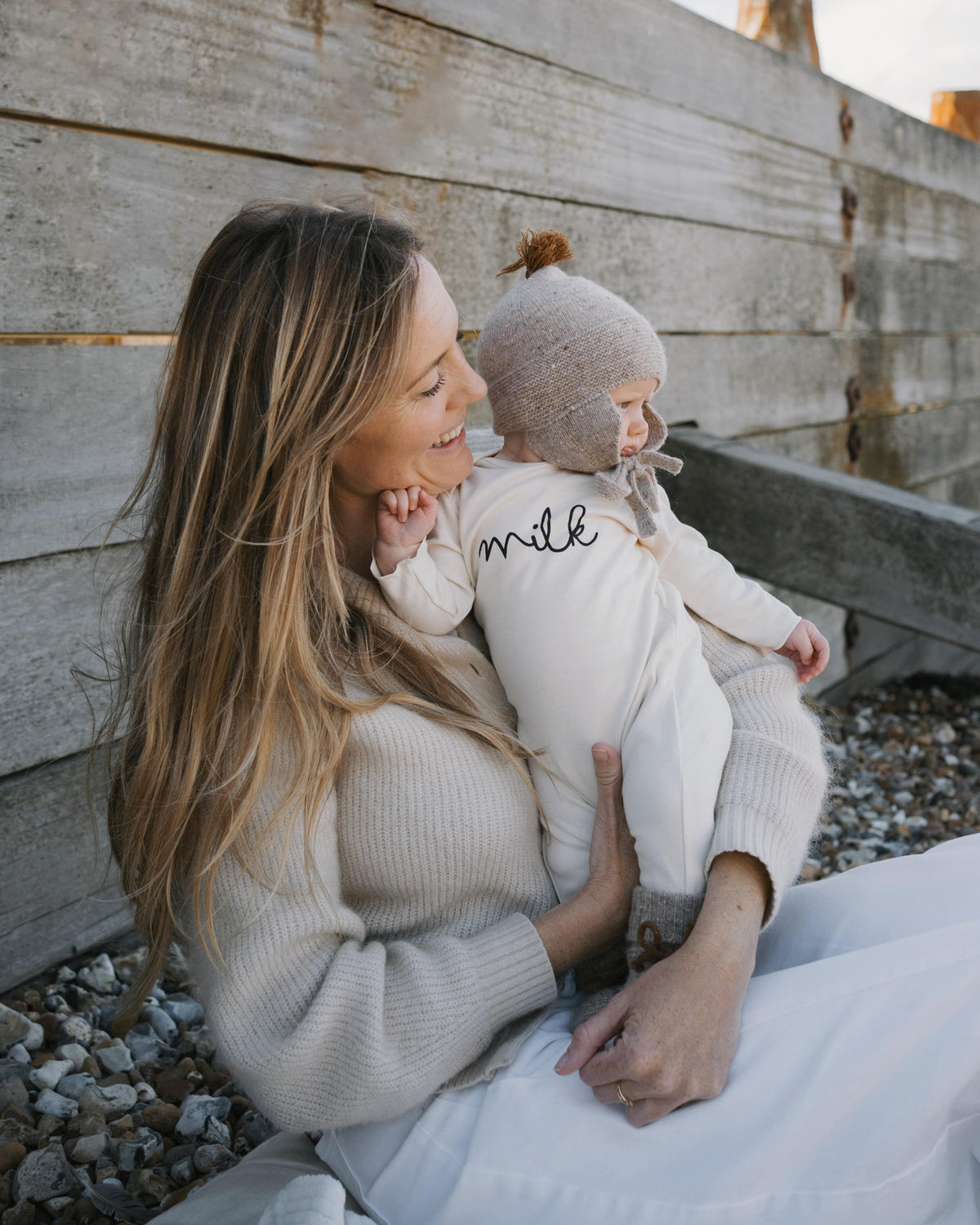 Mom holding a baby in undyed cotton milk playsuit against a wooden wall