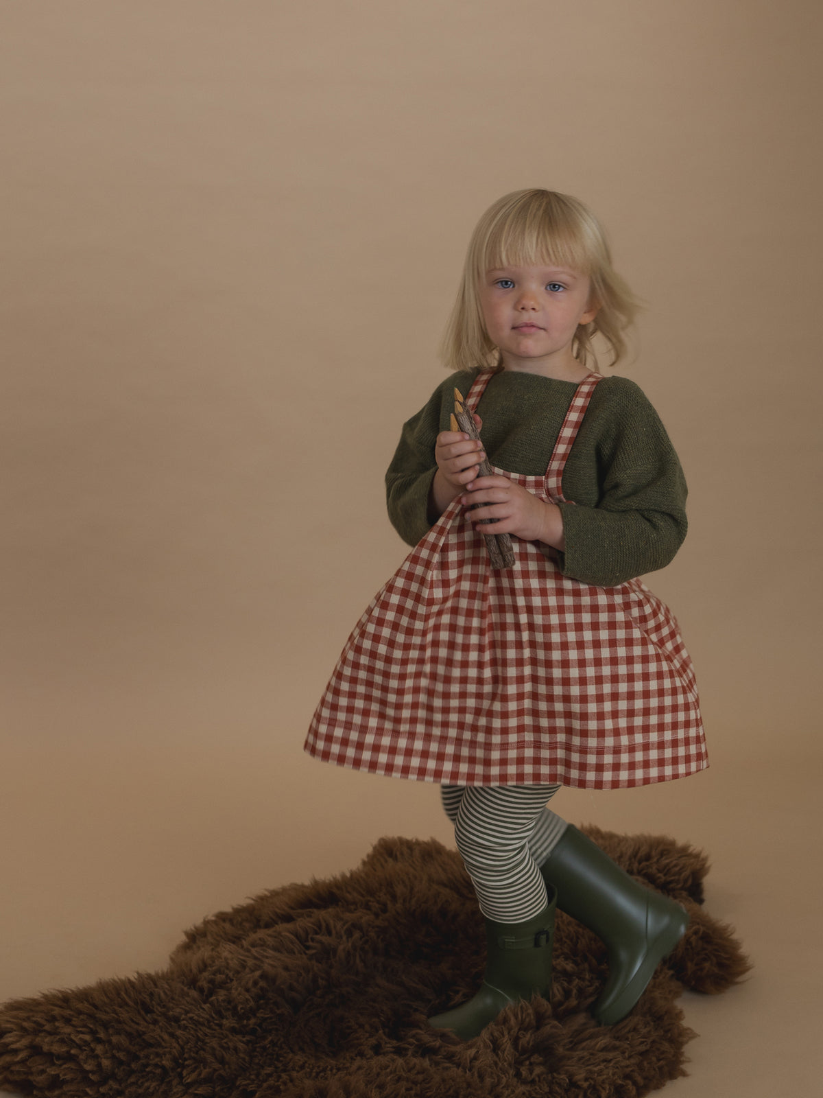 toddler in paprika red gingham pinafore skirt with green wool jumper, and green striped sweatpants