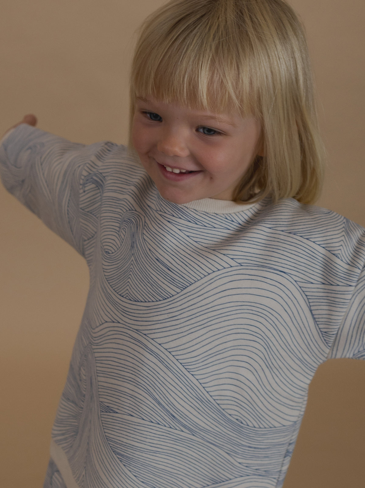 toddler in cotton sweatshirt with Seascape design of blue line-drawn ocean waves standing with arms out