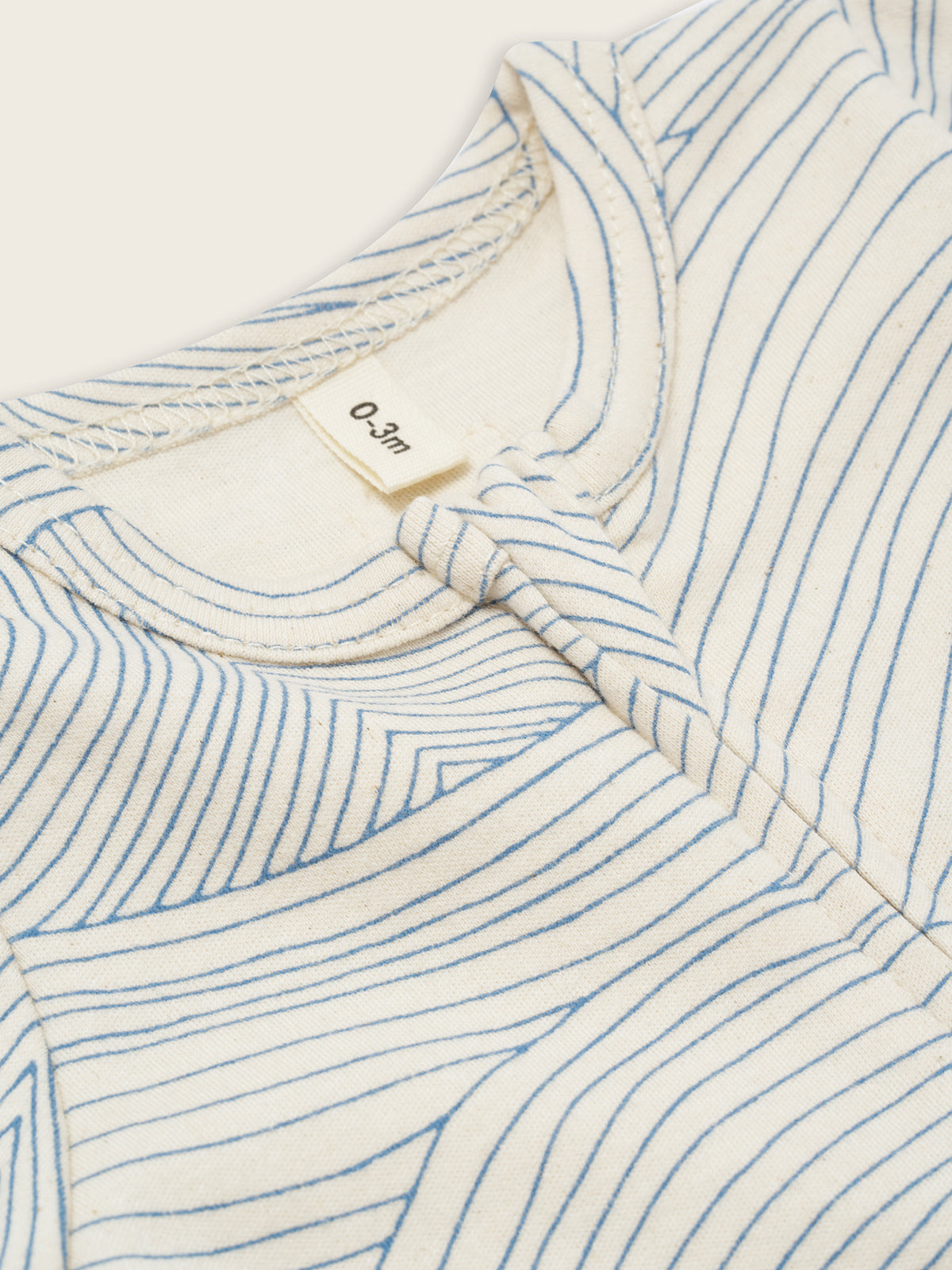 close up of baby cream undyed cotton zip sleepsuit with flowing blue Seascape line-drawn ocean waves