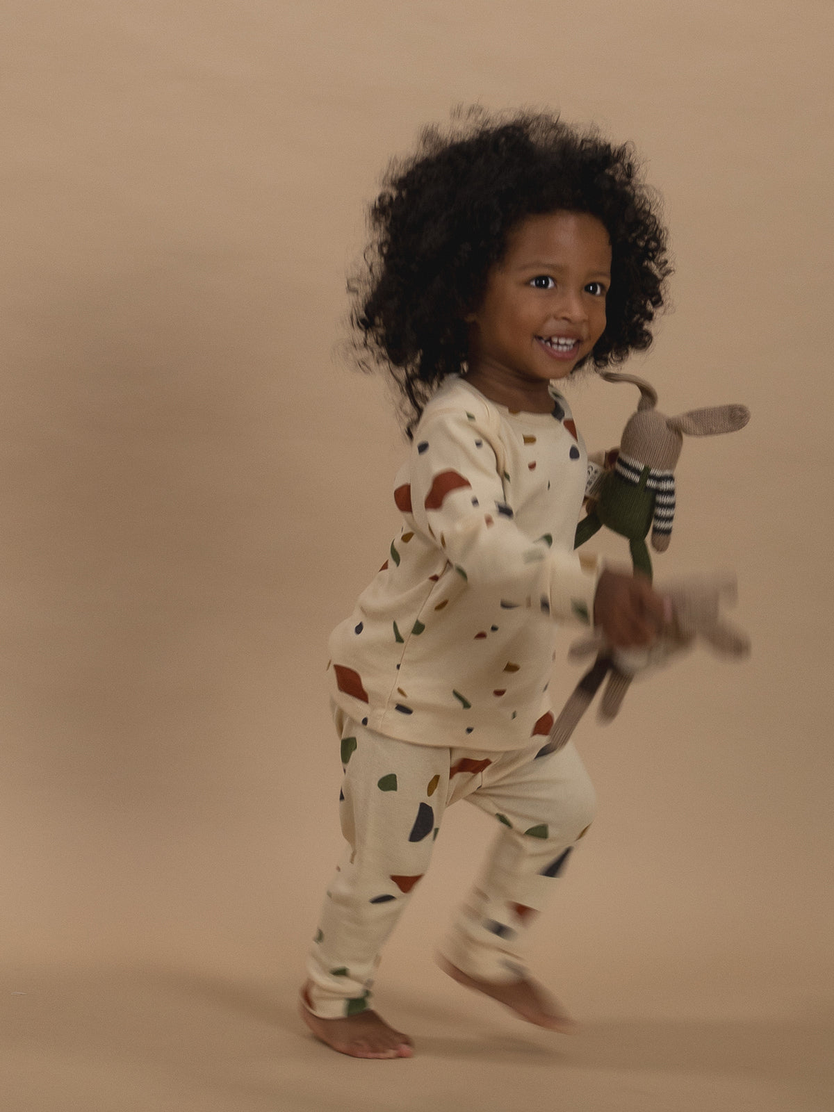 toddler in ribbed cotton long-sleeved top & leggings set with terrazzo print, running with toys