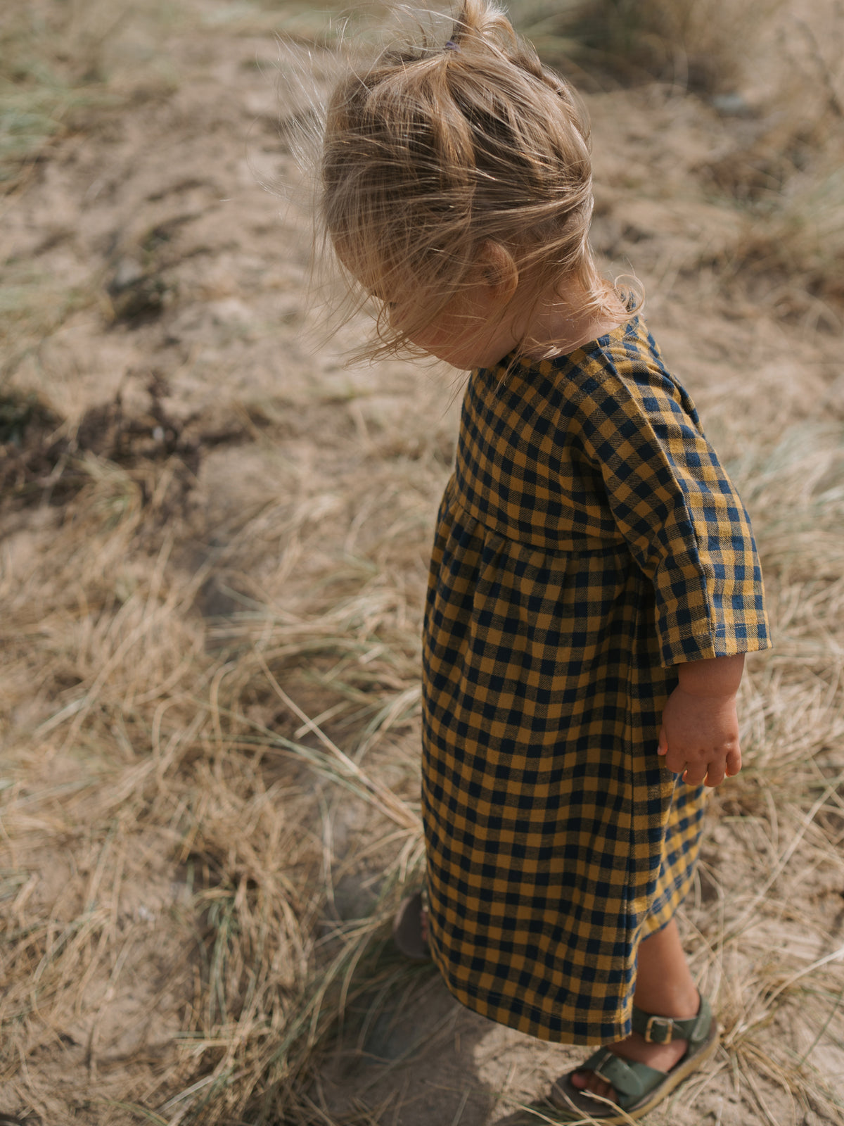 toddler in gingham dress with buttons on the back & gathered waist & green sandals