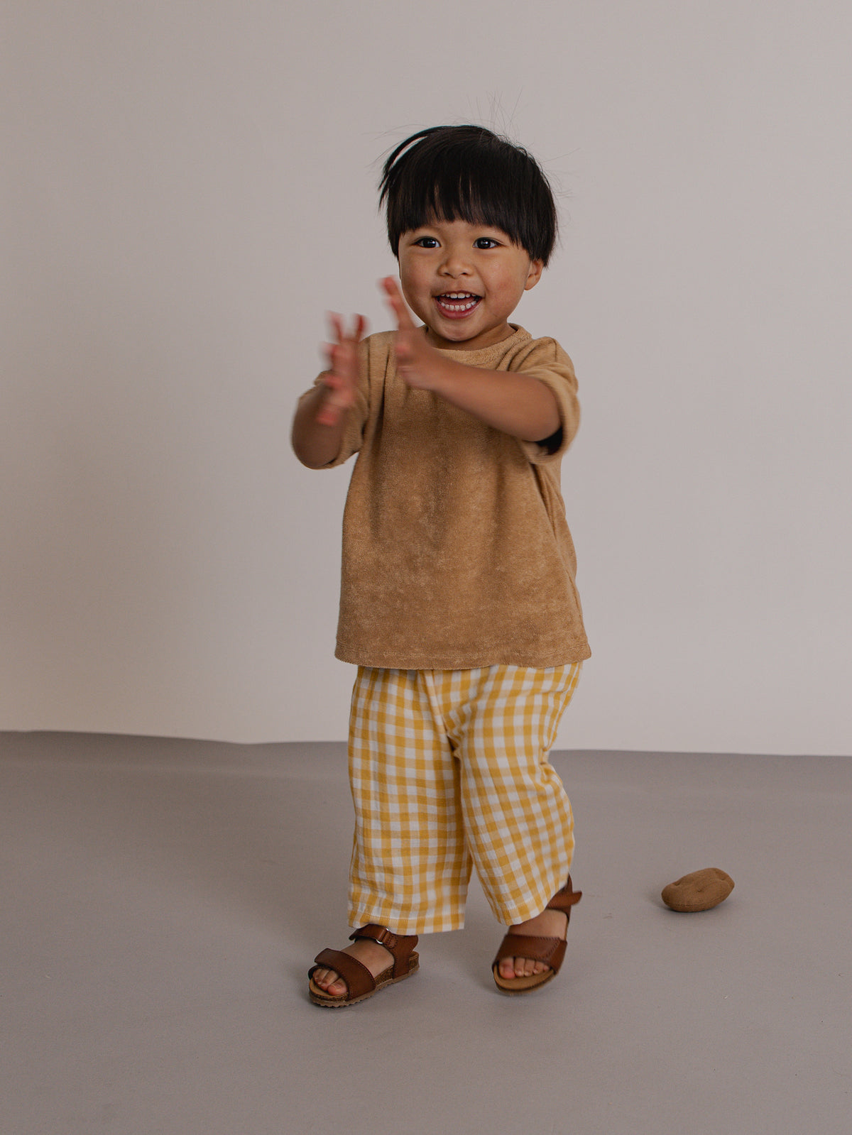 Child wearing a brown shirt and yellow checkered pants on a plain background