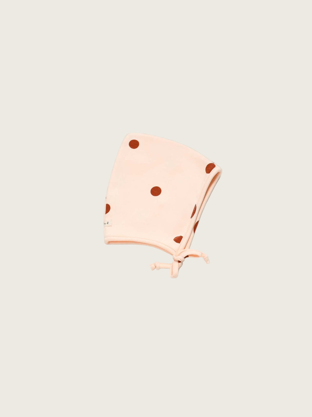 Pink polka dot baby bonnet on a light beige background