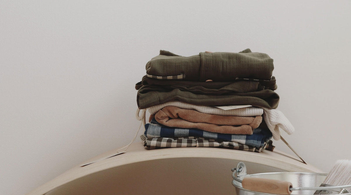 Pile of folded baby clothes with olive, brown, navy gingham, brown gingham colours and patterns
