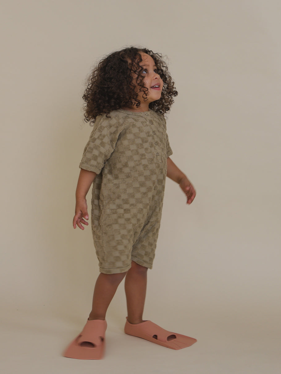 toddler wearing dusky beige checkerboard terry cotton beach romper & flippers looking up