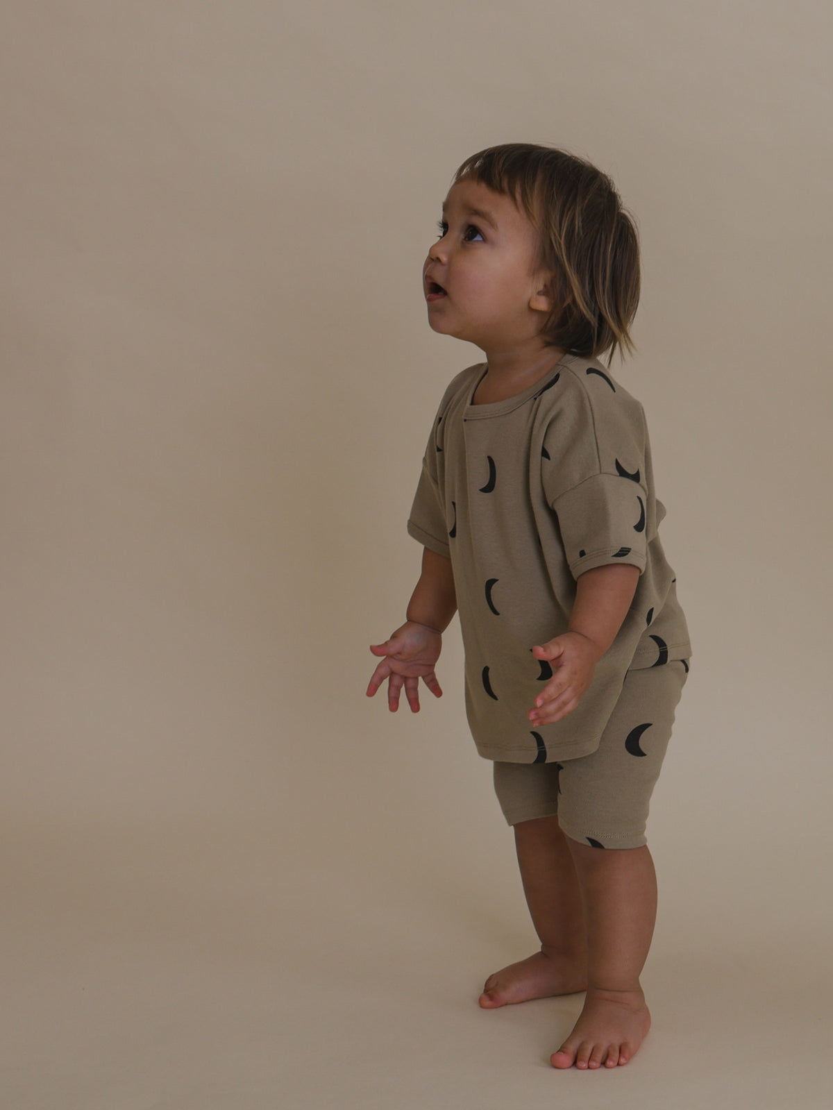 toddler in beige ribbed cotton biker shorts with black moons & matching top looking up