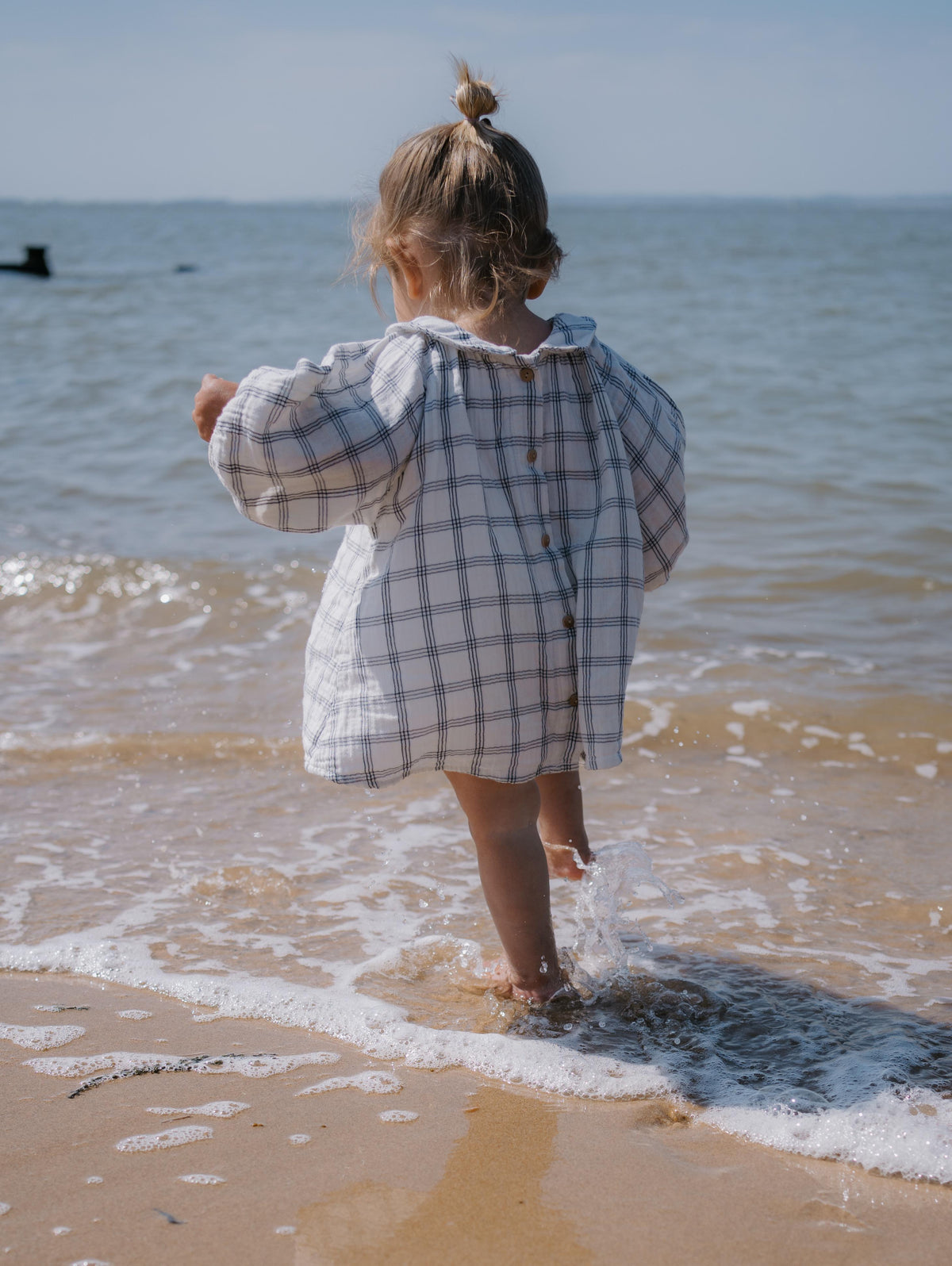 baby girl wearing beach dress  navy window check long sleeved two-way muslin button-down white dress, with peter pan collar & gathered cuffs