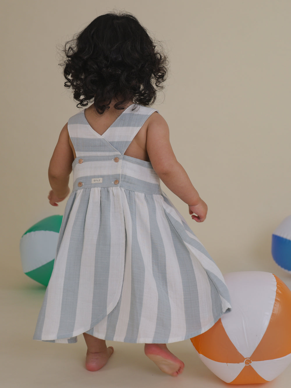 toddler twirling in sardine striped sleeveless dress with button back & curved hem, beach balls on floor