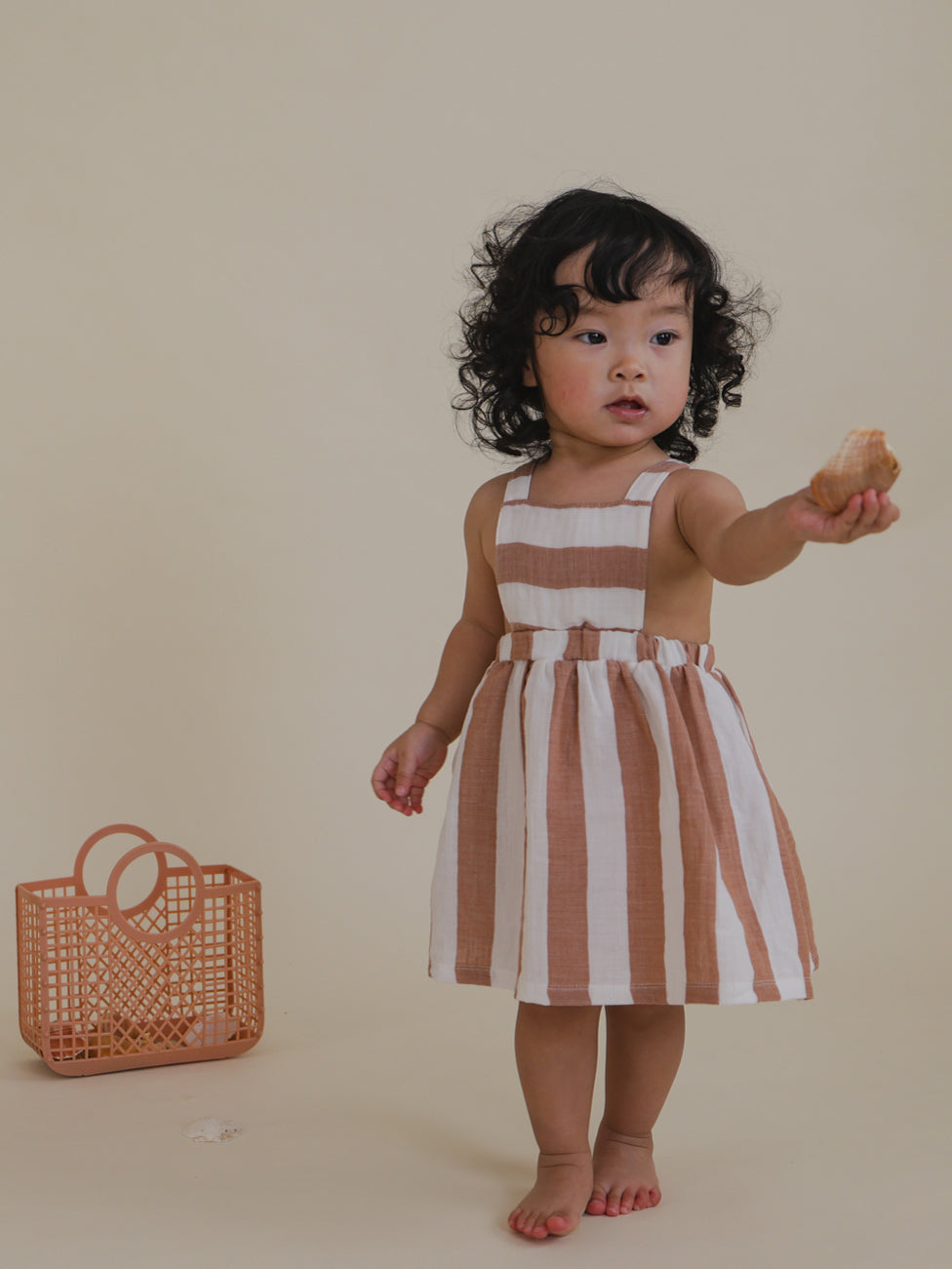 toddler in sienna red striped apron skirt with elastic waistband holding seashell