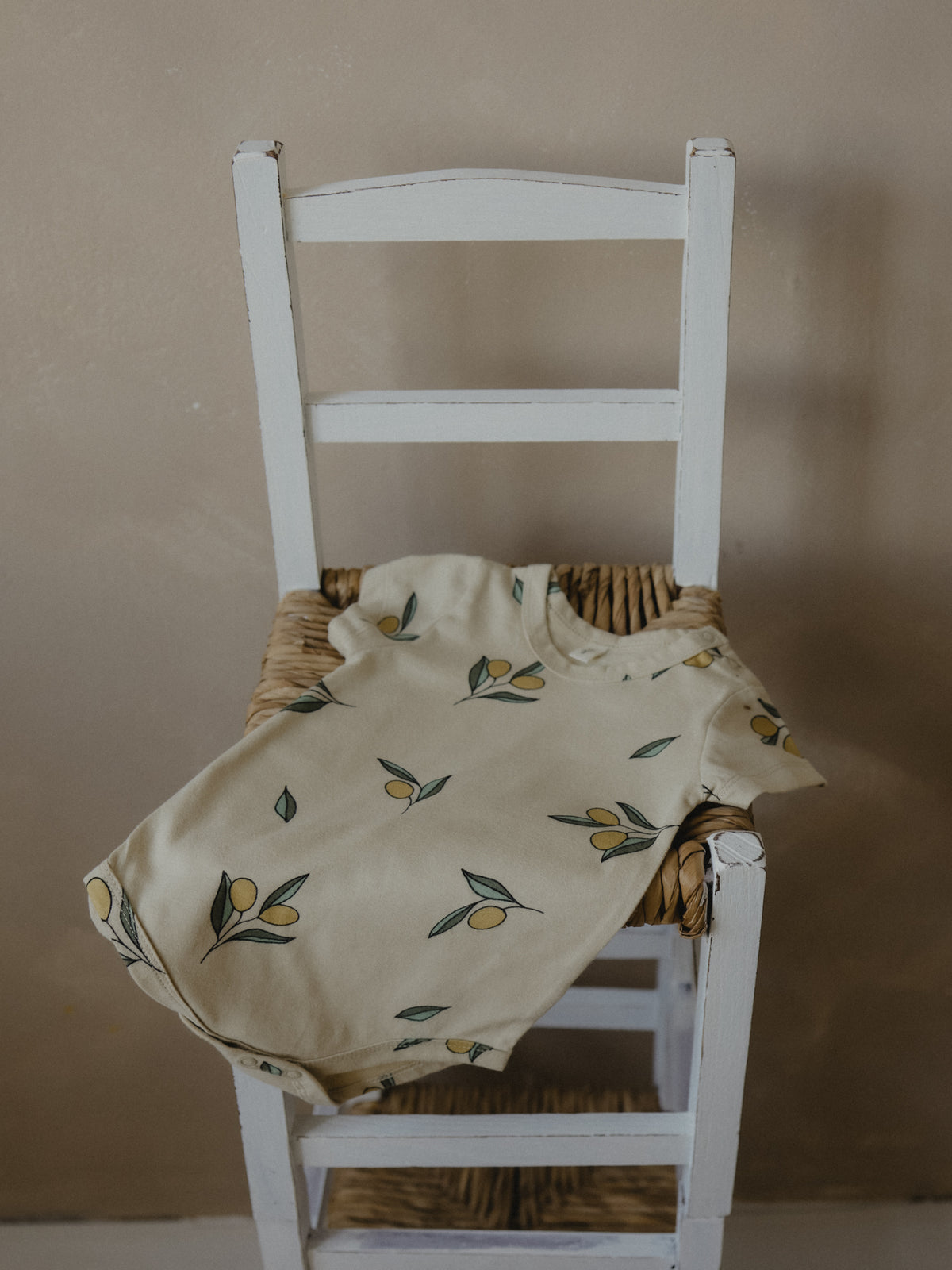 short sleeve baby bodysuit in cream with olives draped over chair