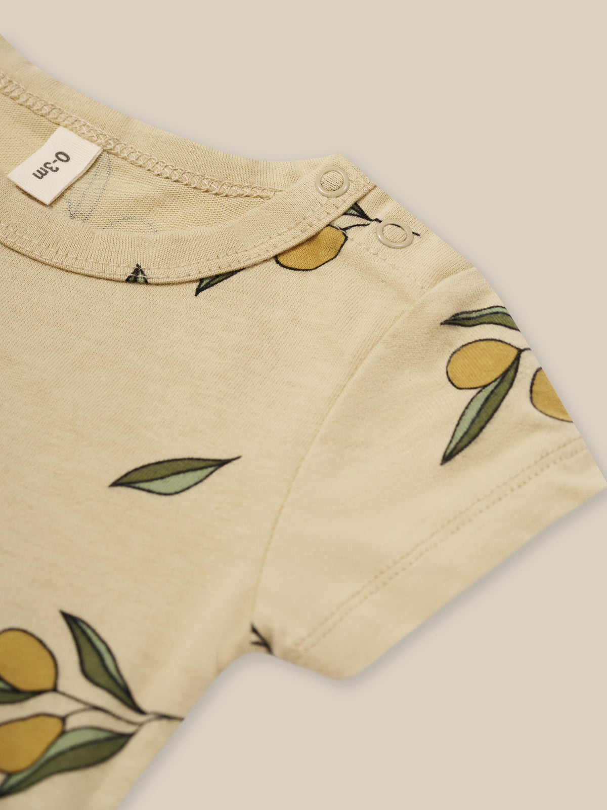 close up of baby organic jersey cotton cream short sleeved bodysuit with olive print & poppers