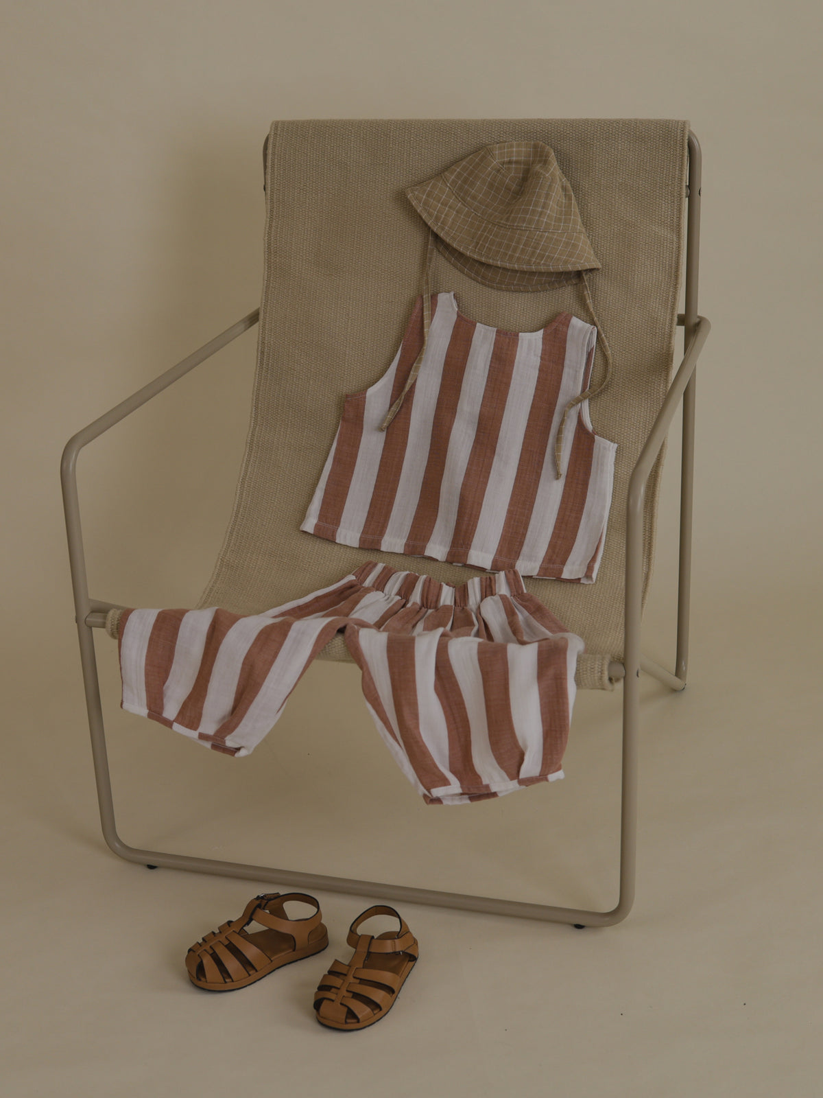 outfit flatlay on chair with sienna red striped muslin resort sleeveless top & pants set, bucket hat