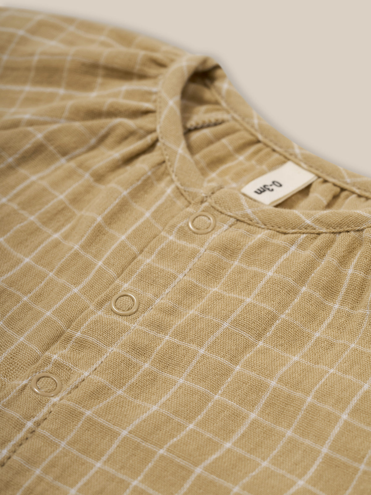 close up of baby wheat gold grid check organic muslin onesie gathered neckline & front poppers