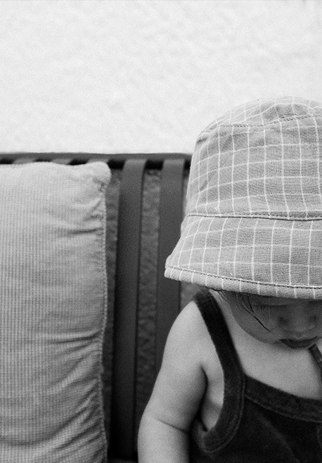 Child wearing a checkered hat sitting on a couch with a neutral background
