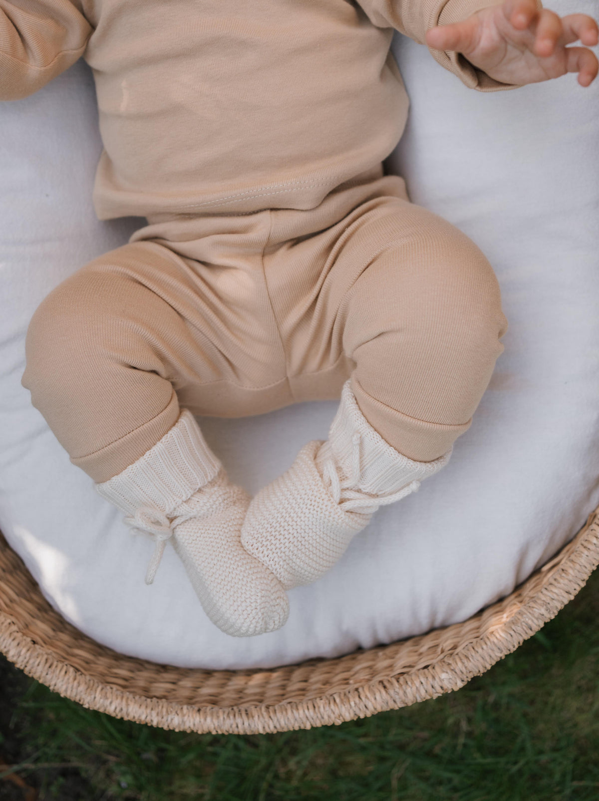 baby wearing undyed cotton knitted booties and matching set wiggling in moses basket