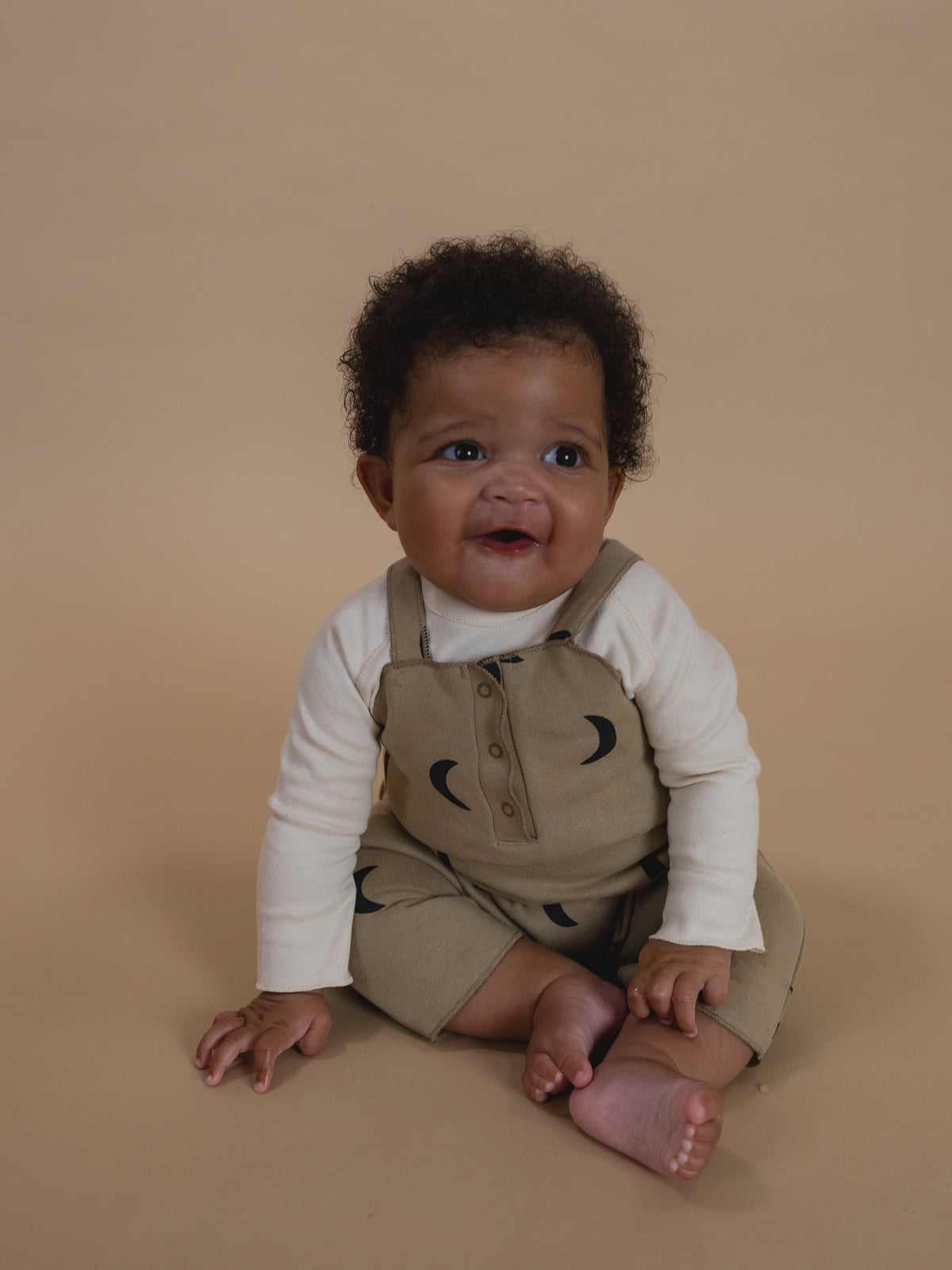 baby in dusky beige terry cotton salopette with black crescent print, and white sweatshirt