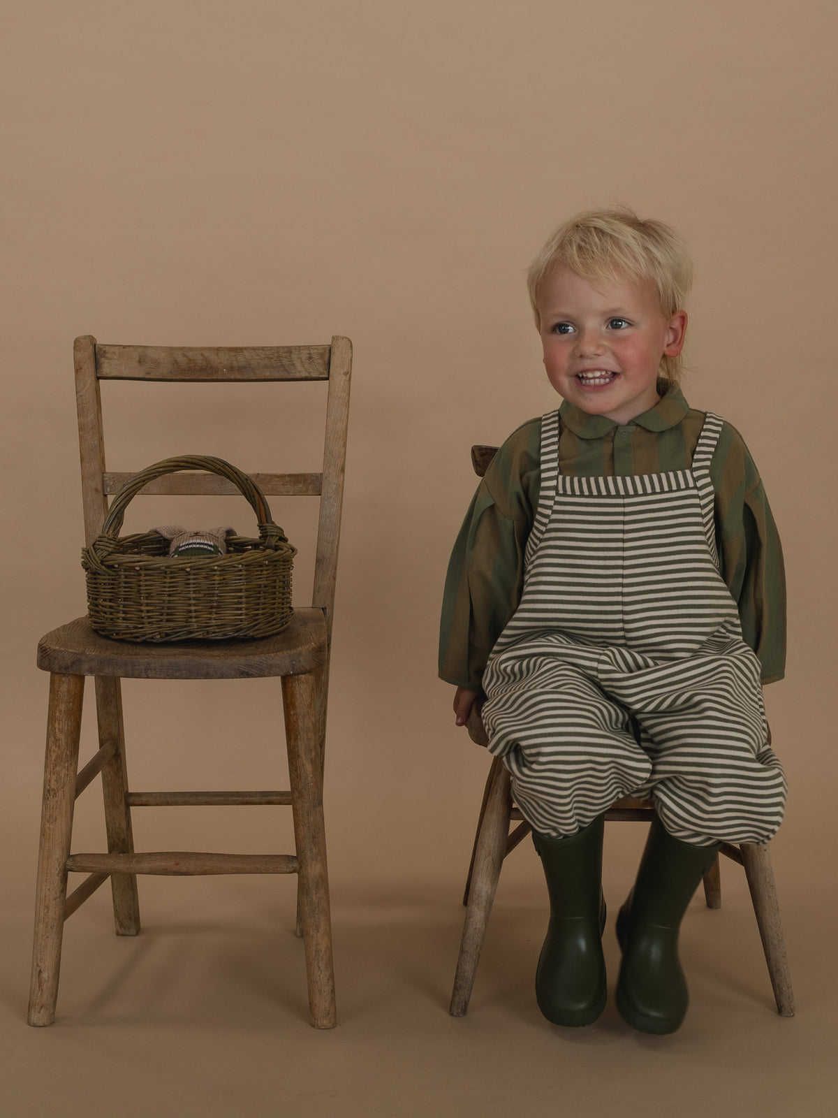 toddler in oversized green and white striped dungarees with lodge shirt sitting on wooden chair