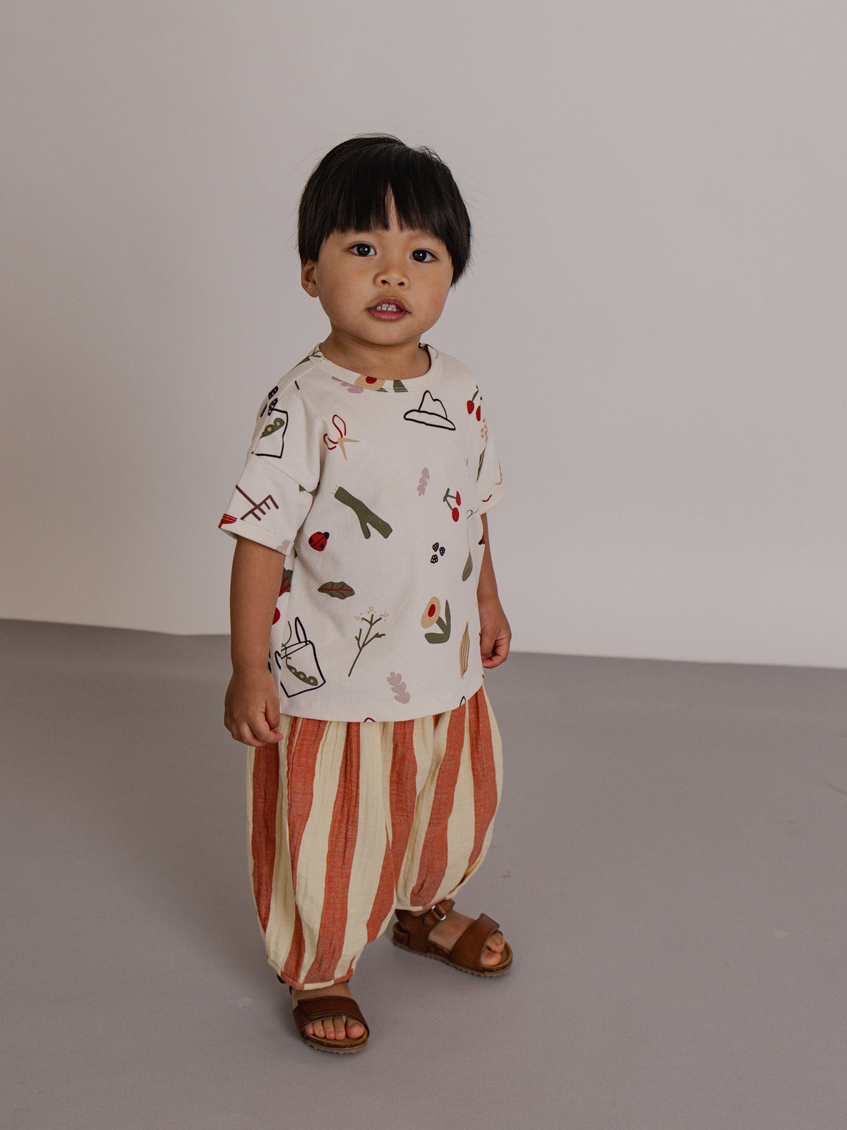 Child wearing a patterned shirt and striped pants standing against a plain background