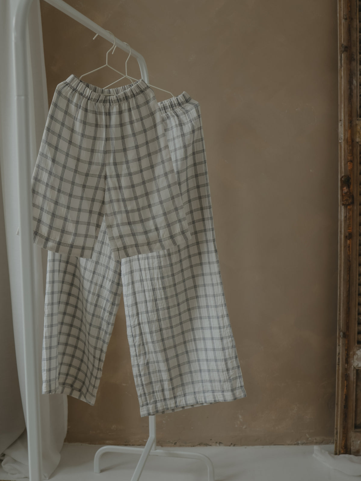 Plaid pants hanging on a white hanger against a beige wall.