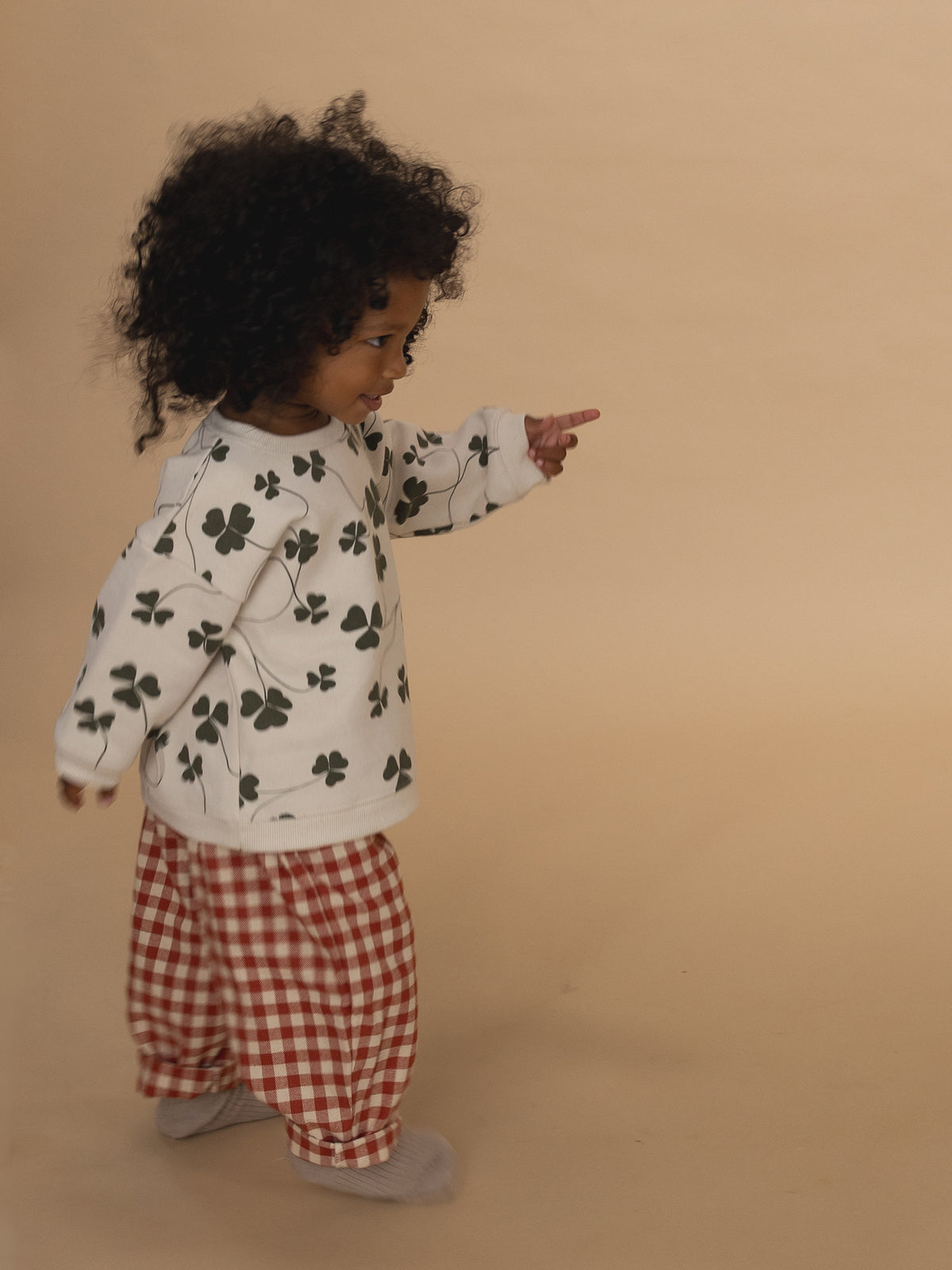 toddler walking in red and cream gingham wide leg flannel pants, and sweatshirt with clover print