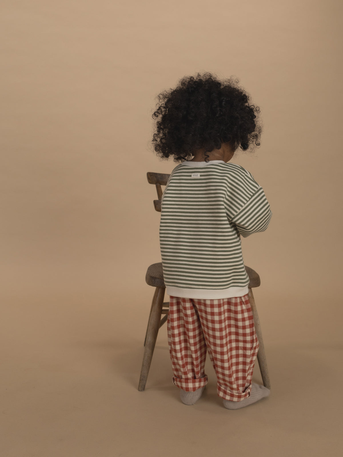back of a toddler in red and cream gingham wide leg flannel pants and green striped sweatshirt
