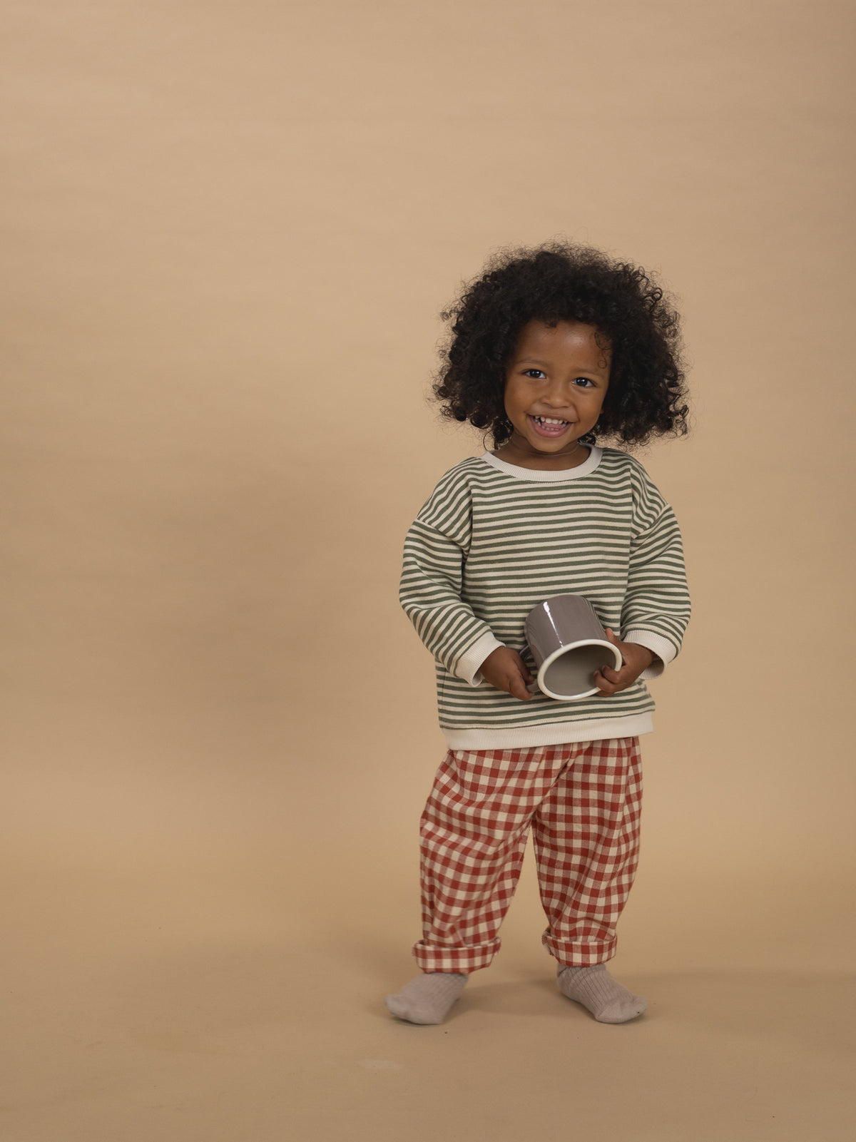 toddler in red and cream gingham wide leg flannel pants and green striped sweatshirt holding cup