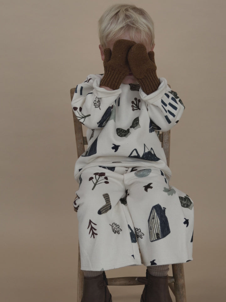 toddler in matching cream cotton sweatshirt and pants with nature-themed graphics, playing peekaboo