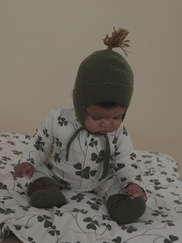 baby in forest wool booties with matching tassel hat, and clover sleepsuit grabbing blanket