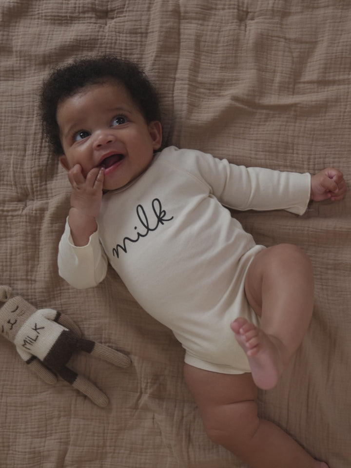 baby wearing cream bodysuit with milk text, lying beside wool plushie with milk embroidery